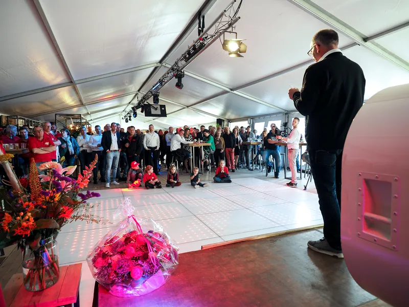 Spreker op een podium voor een volle tent tijdens een bedrijfsevenement