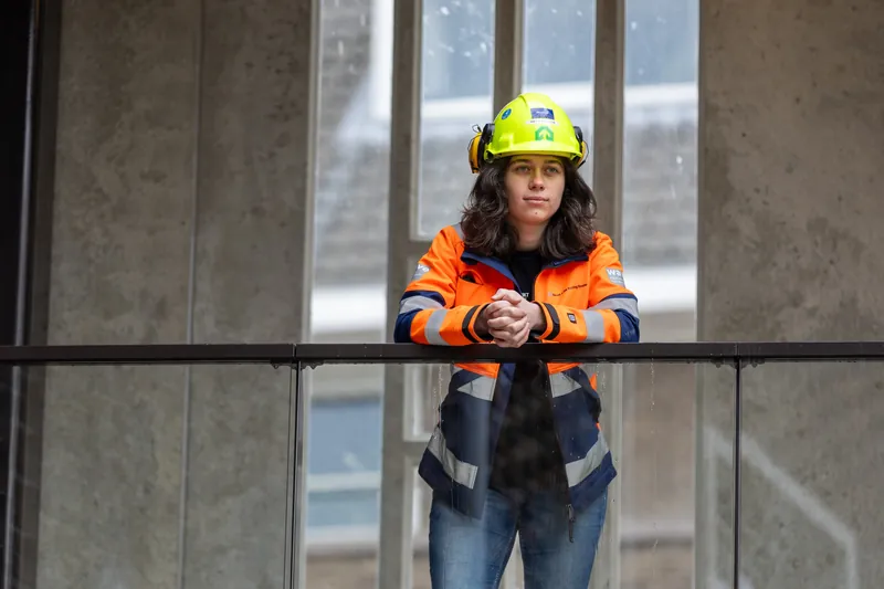 Bedrijfsreportage: bouwprofessional leunt op een glazen balustrade in een gebouw in aanbouw