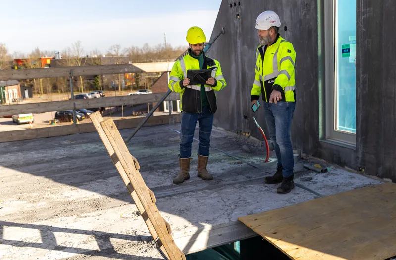 Bedrijfsreportage: twee collega's overleggen op een dak van een bouwproject
