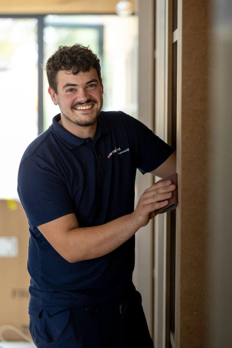 Lachende man in een marineblauw poloshirt die een kozijn schuurt