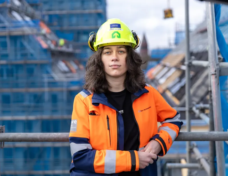 Portret van een bouwprofessional met gele helm en oranje werkjas