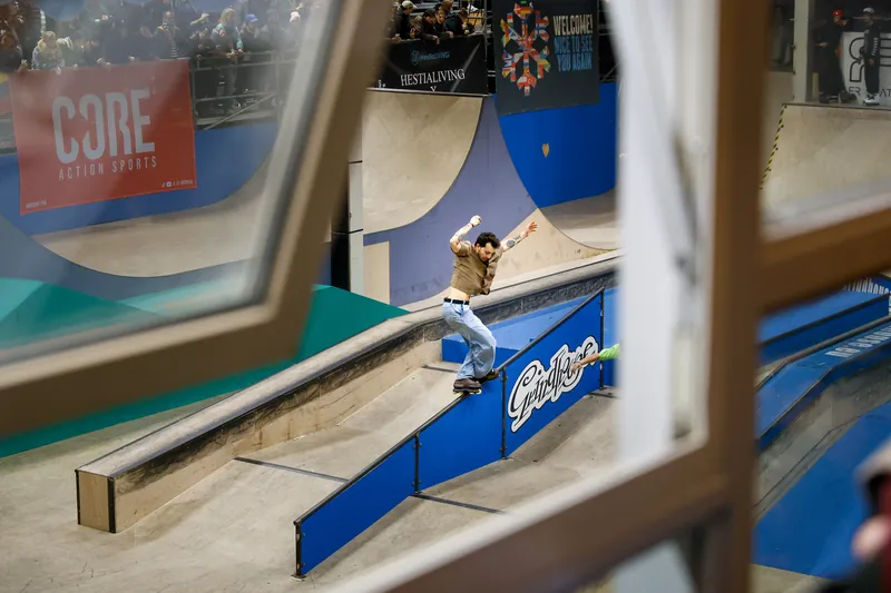 Skater glijdt over een rail in een skatehal, gefotografeerd door een raam