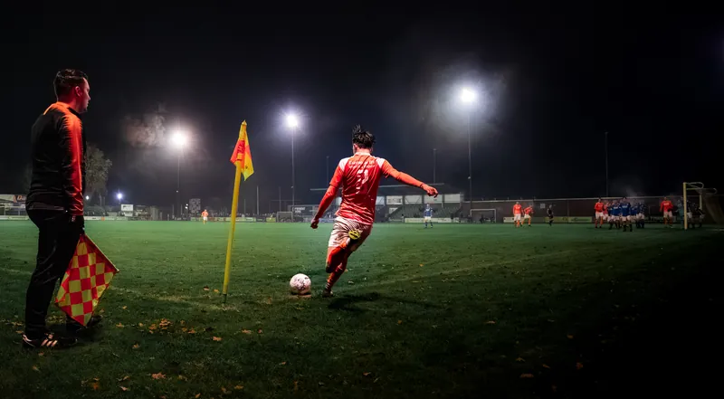 Voetballer neemt een hoekschop bij avondwedstrijd onder lichtmasten