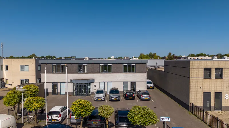 Dronefoto van de voorzijde van een kantoorpand met parkeerplaats en bomen