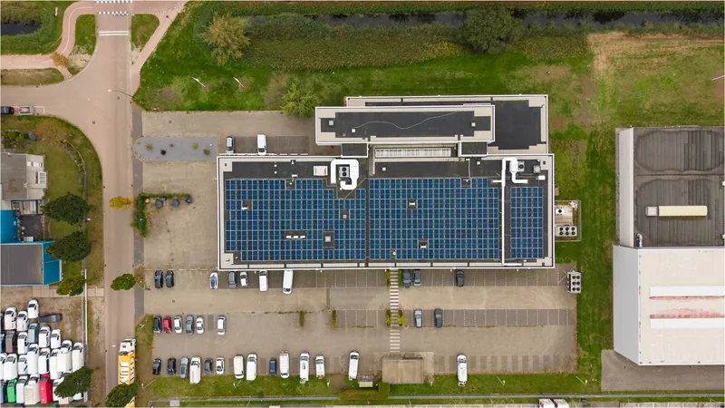 Dronefoto recht van boven op een bedrijfsdak vol zonnepanelen met parkeerplaats